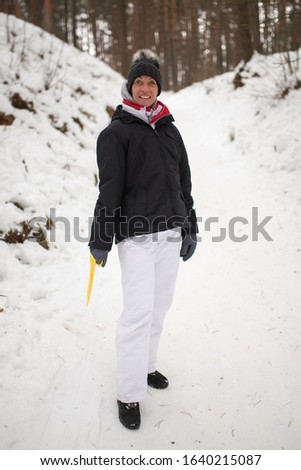 An adult woman with ice sledges in her hands is about to ride a slide.