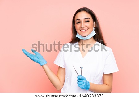 Woman dentist holding tools isolated on pink background holding copyspace imaginary on the palm Royalty-Free Stock Photo #1640233375