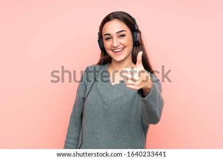 Young caucasian woman isolated on pink background listening music and with thumb up