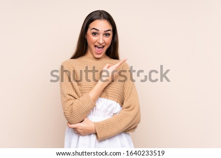 Young caucasian woman isolated on beige background surprised and pointing side