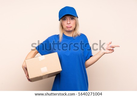 Young delivery woman over isolated background pointing to the laterals having doubts