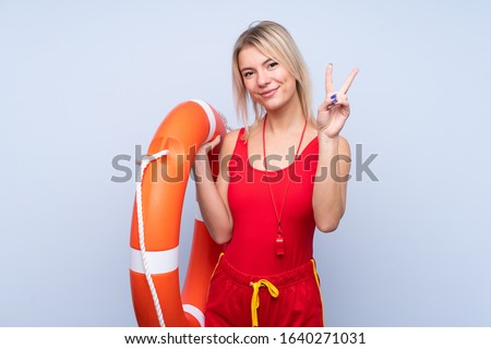 Lifeguard woman over isolated blue background with lifeguard equipment and doing victory sign