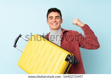 Teenager caucasian man isolated on purple background in vacation with travel suitcase