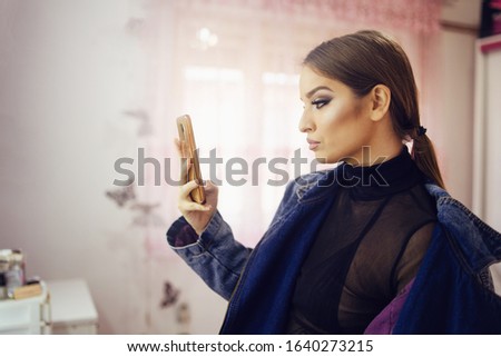 Portrait of young beautiful woman caucasian girl using mobile smart phone camera to take a selfie photo while standing in a room at home