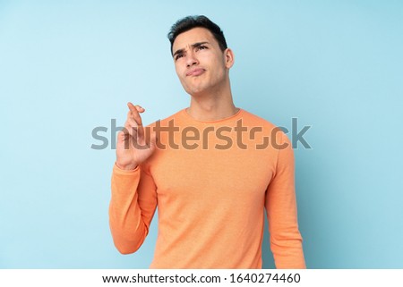 Young caucasian handsome man isolated on blue background with fingers crossing and wishing the best