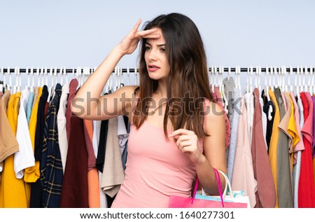 Young caucasian woman buying some clothes in a store looking far away with hand to look something