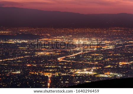 Panoramic night view of urban sprawl in San Jose, Silicon Valley, California; Visible light trail left by cars driving on one of the freeways; long exposure
