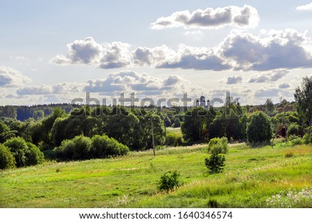 picture of beauty of summer day. Glade, sunlit, green forest. On background of blue sky, dome with crosses of Orthodox Church. Posts with electric wires and hedge. For scenery, postcards.