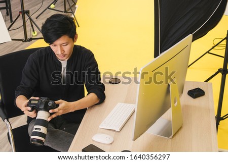 Portrait of young Asian male professional photographer checking picture or image on digital camera while working in the modern studio photo with lighting equipment. Top view photo.