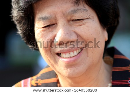 close-up portrait of happy and smiling  attractive senior woman with glasses, delicate facial features looking directly at the camera while standing outside .A female older than 60
