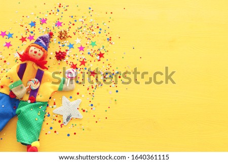 Party colorful noisemaker and cute clown over yellow wooden background . Top view, flat lay
