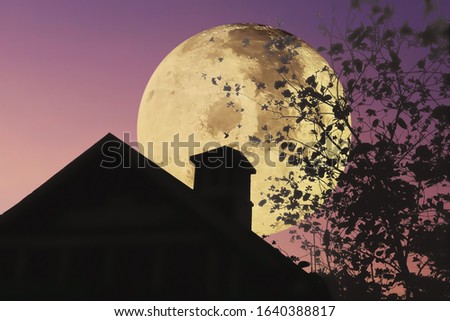 Big moon with silhouette roof of the house chimney and tree leaves on clear and beautiful twilight night sky  background. Image of moon furnished by NASA.
