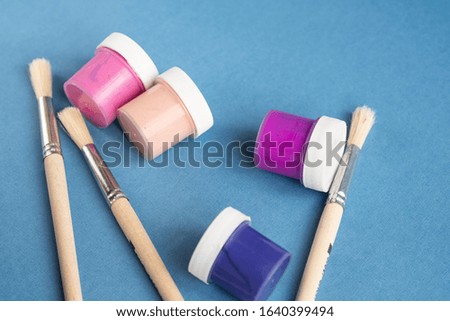 Colorful vibrant cans of gouache paint and brushes isolated on color blue background. Colorful paint cans set, Painting background. A set of acrylic paints in jars for the artist. Copy space.