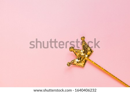 golden magic stick from sequins in crown shape on pastel pink backgeound. Creative flat lay in minimal style