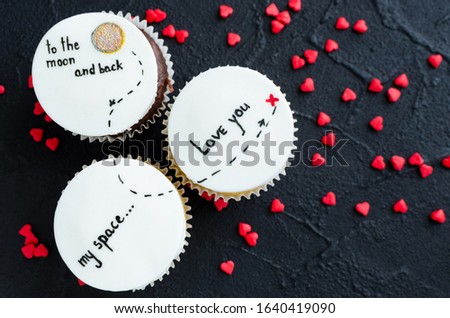 Delicious cupcakes with cute images for Valentine Day on black background. I love you to the moon and back. Romantic love background. Happy Valentines Day. Top view.