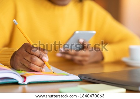 Cropped photo of black girl planning her day, taking notes, using phone