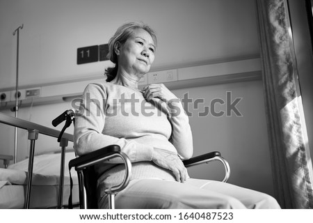 sad and depressed asian senior woman sitting alone in wheel chair in hospital ward or nursing home, black and white