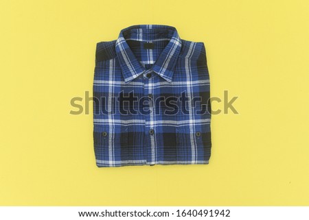 clipping path, top view of folded blue, white \ color plaid shirt isolated on yellow background


