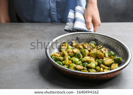 Woman holding pan with roasted Brussels sprouts at light table, closeup