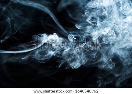 Background image of a wisp of smoke on a dark background. The texture of the flowing smoke. Graphic resources dark backdrop. Texura of white clouds of fog. Curls of smoke frozen in motion.