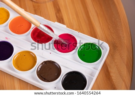Set of watercolor paints, hand holds a brush for painting.