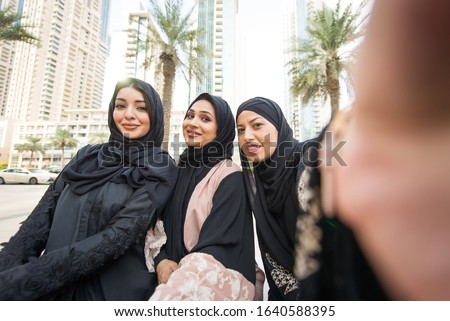Arabic women with abaya bonding and having fun outdoors - Happy middleastern friends meeting and talking while shopping