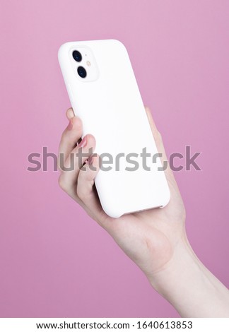 Female hand holding white iPhone 11 back side view. White phone case mock up in female hand isolated on pink background
