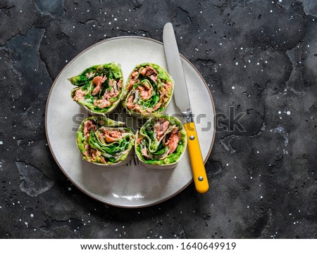 Roasted salmon, avocado puree, green  salad tortilla wrapped roll sandwich on a dark background, top view       