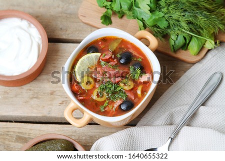 Traditional Russian Solyanka Soup With Beef, Meat, Tongue, Smoked Sausages And Fermented Vegetables Cucucmber And Olives, Served With Slices Of Lemon In Bowl With Sour Cream On Wooden Table. Top View. Royalty-Free Stock Photo #1640655322