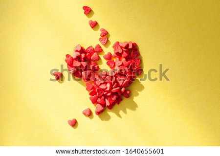 Heart shaped red confetti on a bright yellow background. Top view.