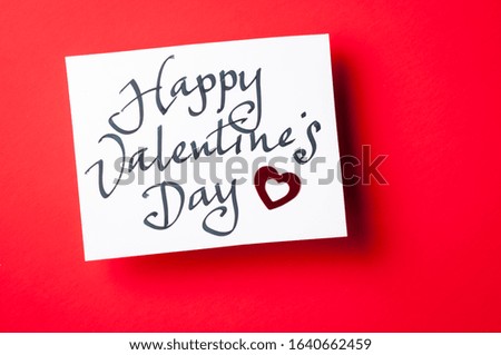 Handwritten Happy Valentine's Day message in informal calligraphic script on white card sitting on red background