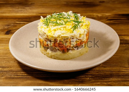 Tasty layered salad with potatoes, chicken breast, marinated mushrooms, carrots, eggs and mayonnaise on wooden table