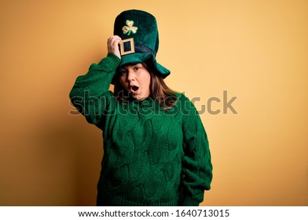 Young beautiful plus size woman wearing green hat with clover celebrating saint patricks day surprised with hand on head for mistake, remember error. Forgot, bad memory concept.