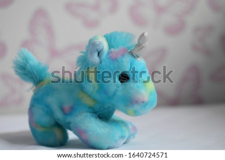 Magical blue unicorn soft toy with glittery unicorn horn. Cute and adorable unicorn teddy sitting on white floor with butterfly background