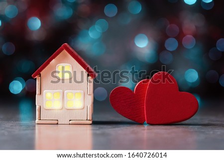 Сozy house with yellow light from window and two red hearts over defocused lights. Valentines day concept