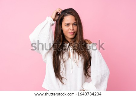 Young Brazilian girl over isolated pink background having doubts while scratching head