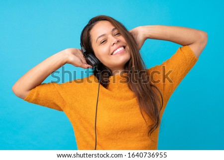 Young woman listening music over isolated blue wall