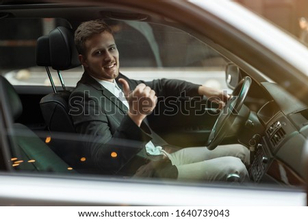 young businessman driving luxury car looking satisfied, showing like sign, successful strategy concept