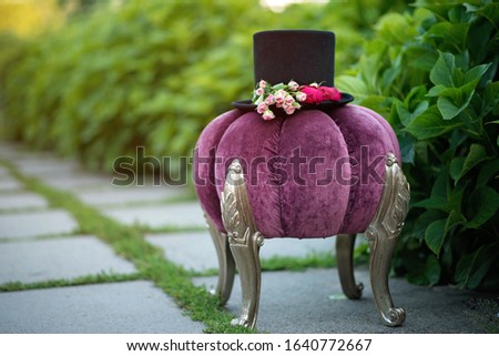 Alice in Wonderland. Hat cylinder decorated with flowers roses on a decorative purple pouf.