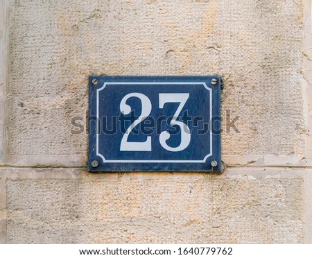 House number 23 White on blue on an old metal limestone wall of a authentic Franch house