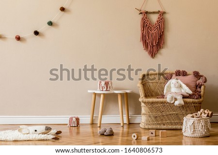 Stylish and cute scandinavian decor of newborn baby room with natural toys, hanging decor balls, macrame, pouf, plush animals and teddy bears. Beige walls. Interior design of kid room. Home staging.
