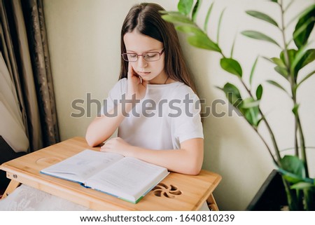 High school girl student at home and distance learning. Performs homework, reads tasks in the book and thinks about their solution. Alternative home teaching. Generation Z