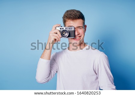 Traveler and photographer. Studio portrait of handsome young man holding photocamera taking photo. Blue blackground.