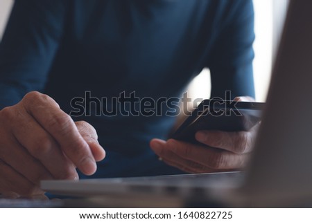 Close up of casual business man using mobile phone browsing internet, working via laptop computer on table at home office, student studying online, E-learning, telecommuting, work from home concept