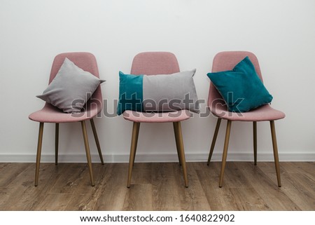 Different pillows on three pink chairs in room, against white wall background