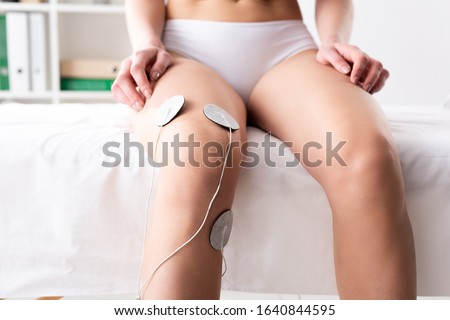 Cropped view of woman with electrodes on knee sitting on massage couch during electrotherapy in clinic