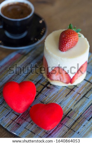Tasty cream strawberry cake with red heart-shapes and coffee. Valentine's Day, love, birthday, celebration concepts. Vertical close-up.