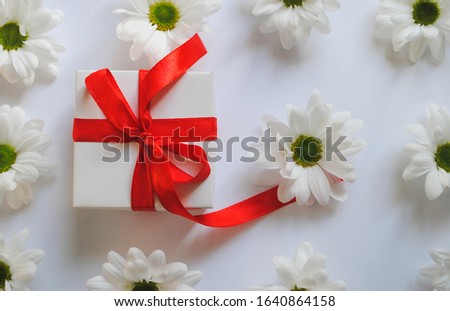 on a white background are white daisies with green centers and a white festive gift box with a red ribbon lies on them. for banners flyers advertising labels and splash screens signage