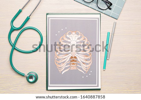 Stethoscope with drawing of human ribs on wooden background