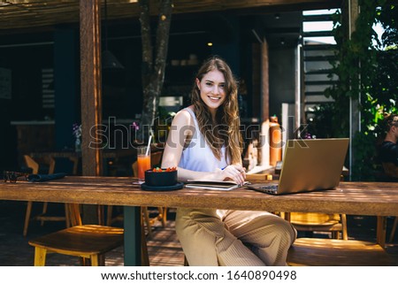 Smiling female freelance writer sitting in cafe at table with drink and laptop and taking notes in notebook while looking at camera on dark background Royalty-Free Stock Photo #1640890498